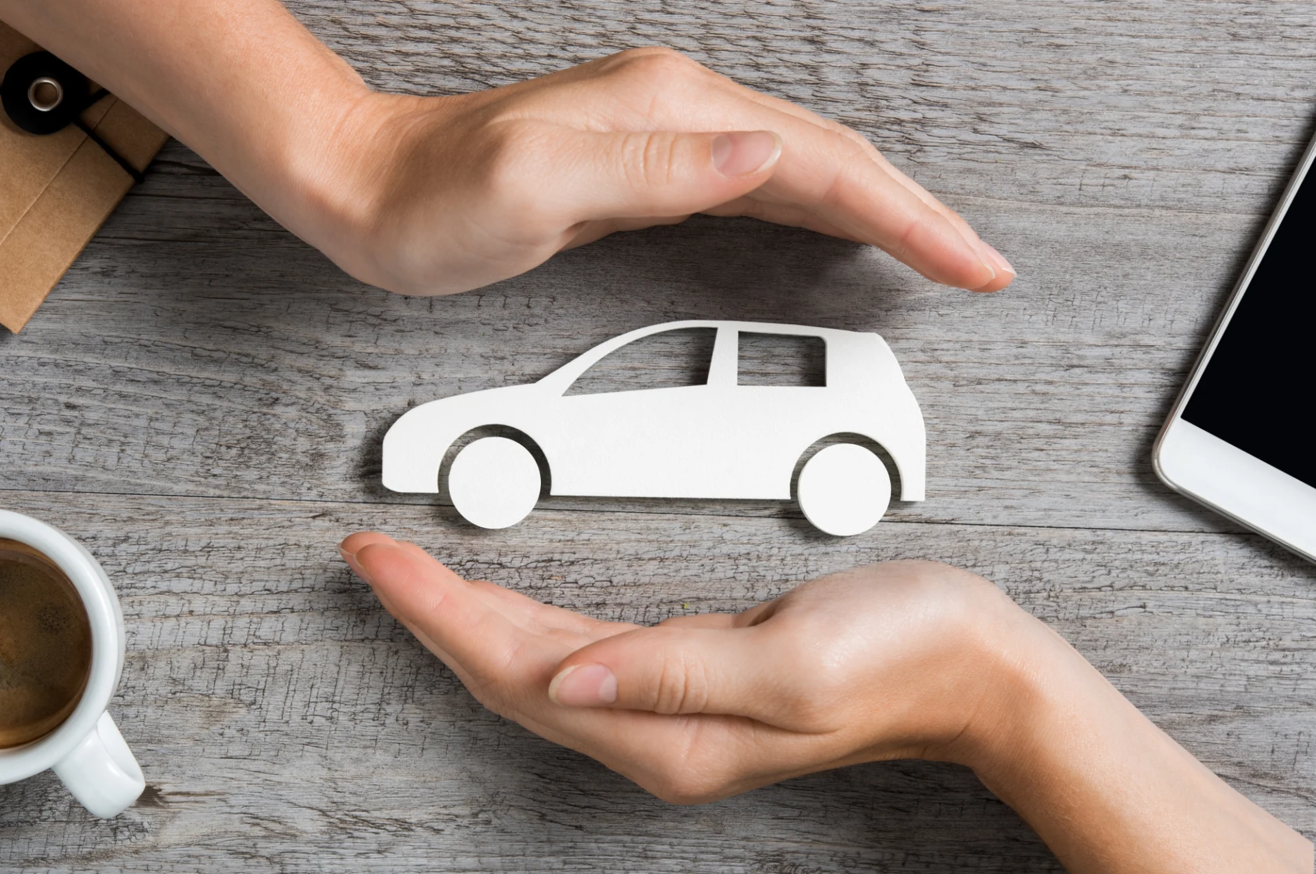 Hands protecting a paper car cutout.